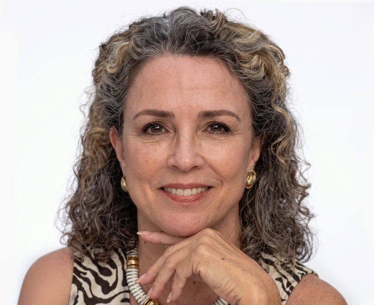 Professional studio portrait of a woman wearing a animal print blouse and gold jewelry against a white background.