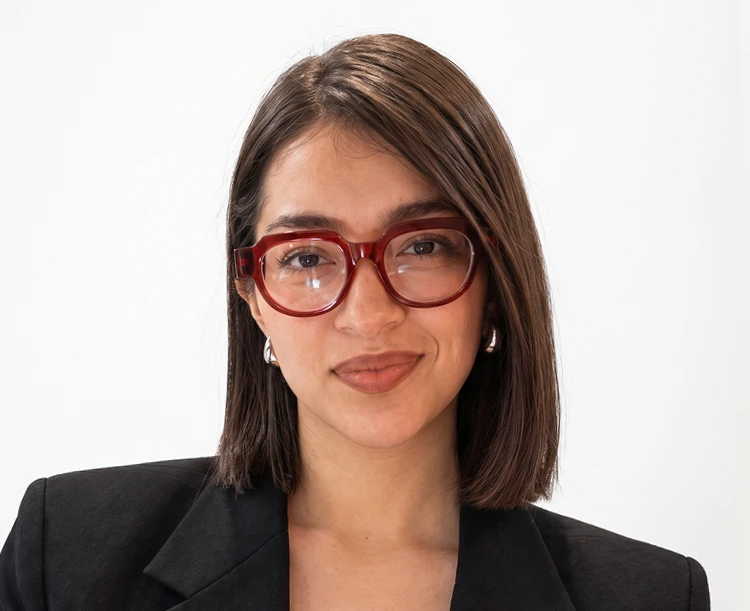 Portrait of a person wearing red glasses and a black blazer against a plain white background.