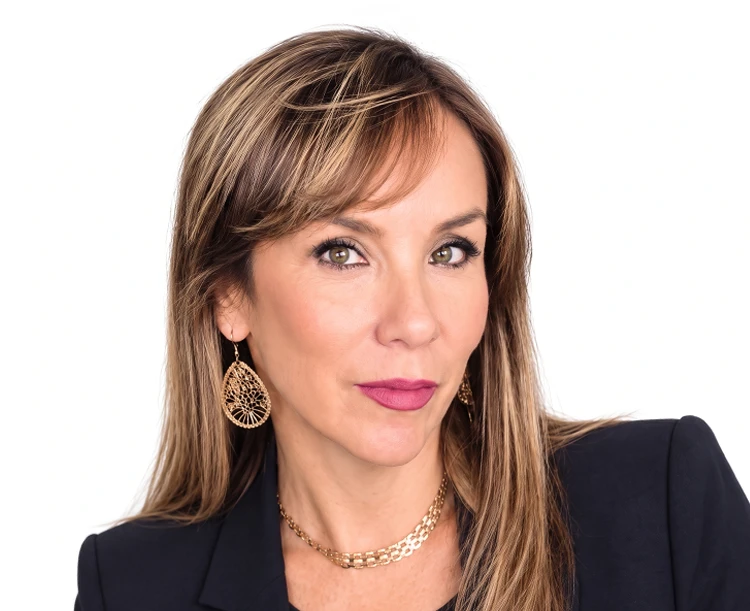 Professional studio portrait of a woman wearing a dark blazer and gold jewelry against a white background.